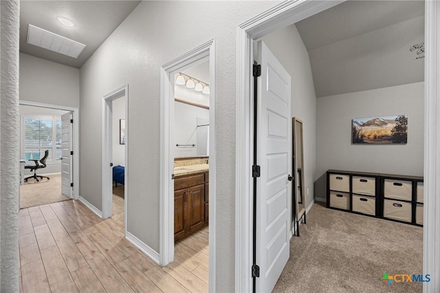 hallway with visible vents, baseboards, lofted ceiling, and light wood-style floors