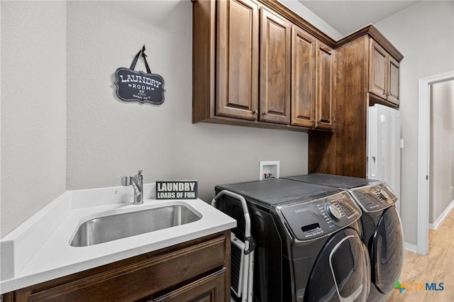 laundry area with light wood-type flooring, independent washer and dryer, a sink, cabinet space, and baseboards