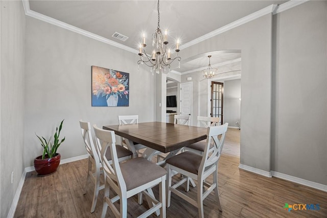 dining area with wood finished floors, baseboards, visible vents, arched walkways, and a chandelier