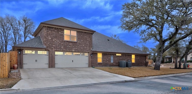 traditional-style home with central air condition unit, driveway, fence, roof with shingles, and brick siding