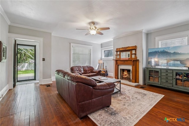 1004 Mitchell St, Gonzales, TX 78629 - living room featuring ceiling fan, dark wood-type flooring, a warm lit fireplace, and crown molding
