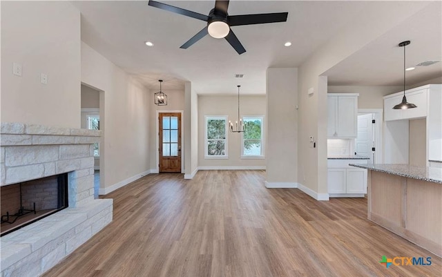 1435 Redwood Rd, Fischer, TX 78623 - unfurnished living room with light wood-style flooring, baseboards, ceiling fan, a stone fireplace, and a chandelier