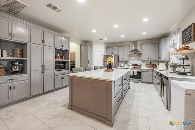 kitchen featuring sink, a center island, appliances with stainless steel finishes, gray cabinets, and wall chimney range hood