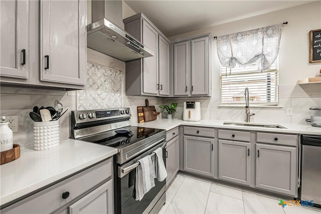 kitchen with sink, wall chimney range hood, gray cabinets, stainless steel appliances, and backsplash