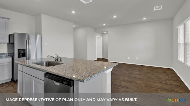 kitchen with light stone counters, stainless steel appliances, a kitchen island with sink, sink, and dark hardwood / wood-style floors