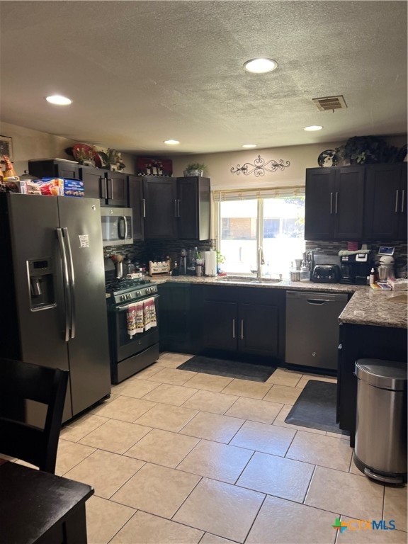 kitchen featuring stainless steel appliances, backsplash, a textured ceiling, light tile patterned floors, and sink