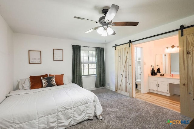 carpeted bedroom with ensuite bath, a barn door, and ceiling fan