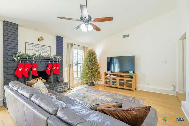 living room featuring light wood-type flooring, a brick fireplace, lofted ceiling, and ceiling fan