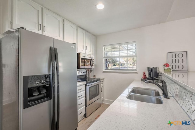 kitchen with light stone countertops, sink, white cabinets, and appliances with stainless steel finishes