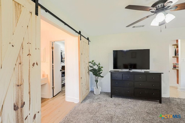 bedroom featuring ceiling fan, a barn door, light colored carpet, and connected bathroom