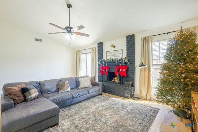 living room with hardwood / wood-style flooring, a brick fireplace, ceiling fan, and vaulted ceiling