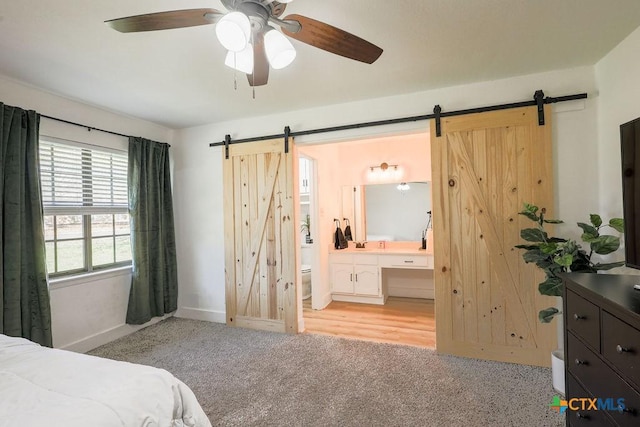 carpeted bedroom with ceiling fan, a barn door, and ensuite bath