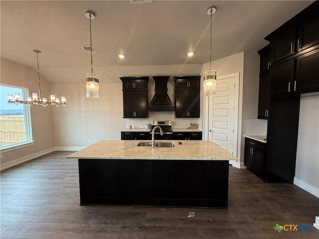 kitchen featuring premium range hood, sink, light stone counters, a center island with sink, and decorative backsplash