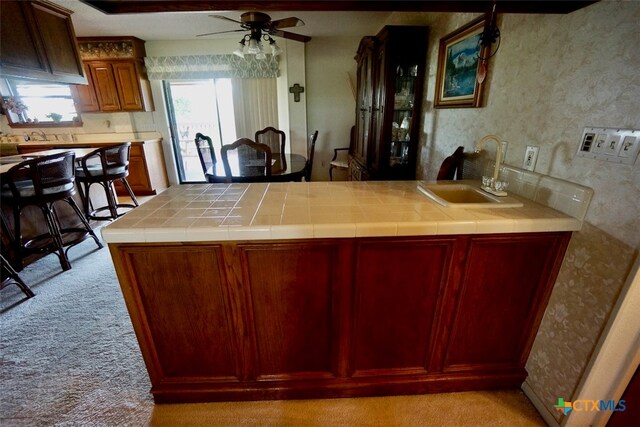 kitchen featuring tile counters, ceiling fan, light carpet, and sink