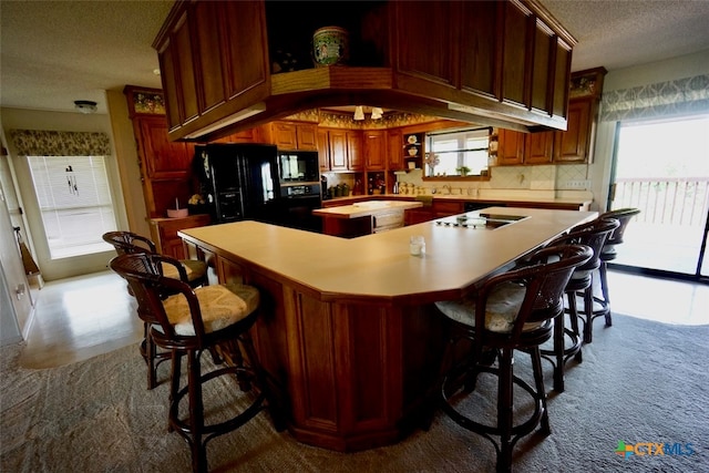 kitchen featuring a wealth of natural light, a kitchen bar, a textured ceiling, and black appliances