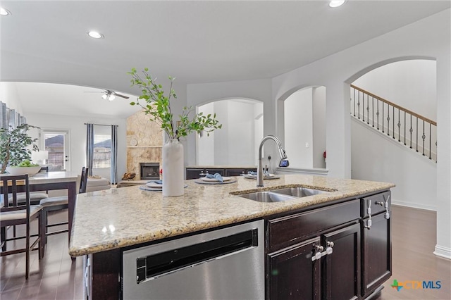 2474 Santa Barbara Loop, Round Rock, TX 78665 - kitchen with dishwasher, a sink, a ceiling fan, a stone fireplace, and a kitchen island with sink