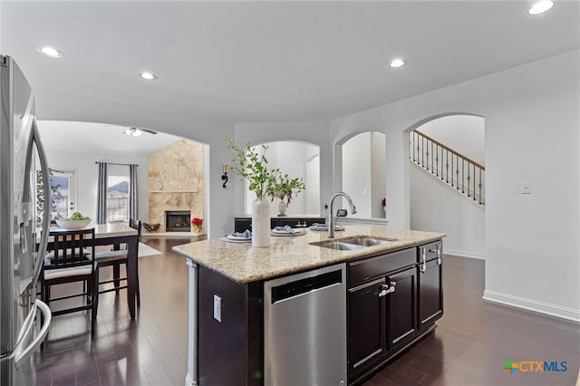 2474 Santa Barbara Loop, Round Rock, TX 78665 - kitchen featuring appliances with stainless steel finishes, a sink, a fireplace, dark wood-style floors, and light stone counters