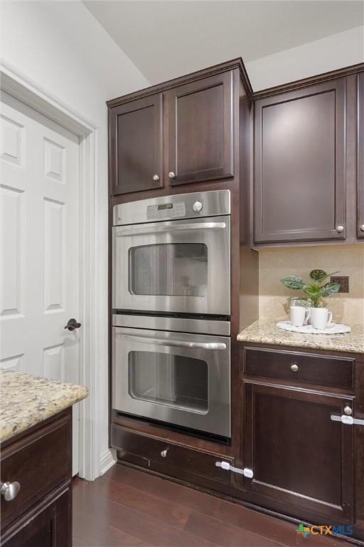 2474 Santa Barbara Loop, Round Rock, TX 78665 - kitchen with double oven, dark brown cabinetry, light stone counters, and dark wood finished floors
