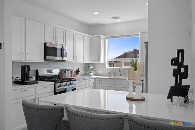 kitchen with a sink, visible vents, white cabinets, appliances with stainless steel finishes, and decorative backsplash