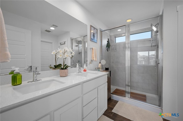 full bathroom with double vanity, wood finished floors, a sink, and a shower stall