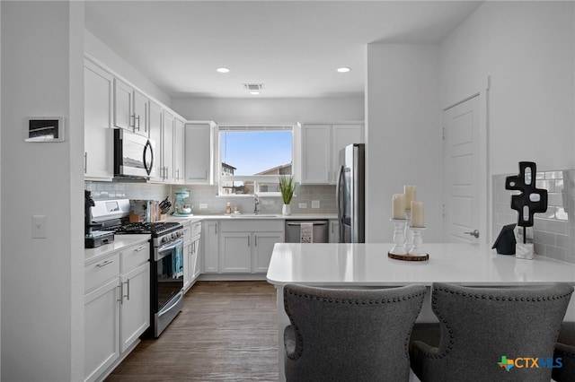 kitchen with visible vents, appliances with stainless steel finishes, white cabinetry, a sink, and a peninsula