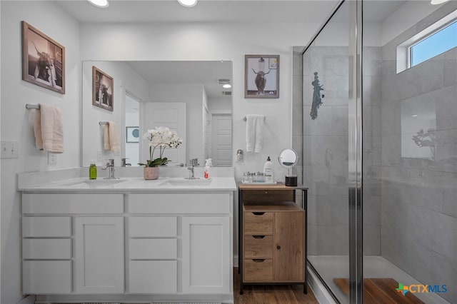 full bath with double vanity, a stall shower, a sink, and wood finished floors