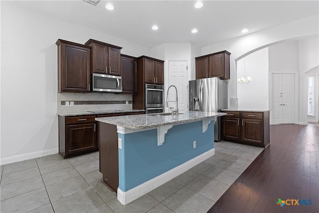 kitchen with decorative backsplash, appliances with stainless steel finishes, a kitchen breakfast bar, a kitchen island with sink, and light tile patterned floors