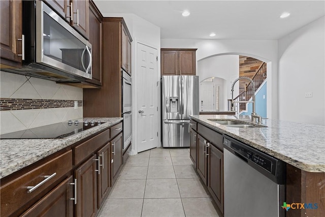 kitchen featuring sink, decorative backsplash, a center island with sink, light tile patterned floors, and appliances with stainless steel finishes