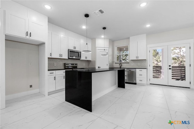 kitchen featuring appliances with stainless steel finishes, white cabinetry, hanging light fixtures, backsplash, and a center island