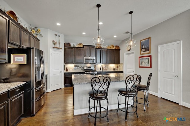 kitchen with decorative light fixtures, an island with sink, stainless steel appliances, and dark hardwood / wood-style floors