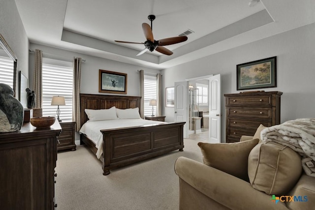 bedroom featuring light carpet, a tray ceiling, ceiling fan, and ensuite bathroom