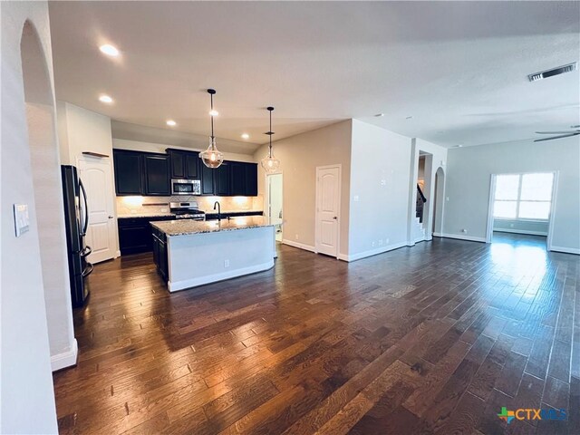 kitchen featuring a kitchen island with sink, dark wood-type flooring, stainless steel appliances, and decorative light fixtures