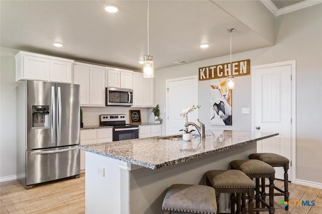 kitchen with light wood-style flooring, stainless steel appliances, white cabinets, tasteful backsplash, and a kitchen bar