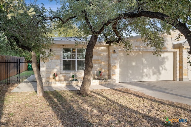 single story home featuring driveway, stone siding, an attached garage, a standing seam roof, and fence