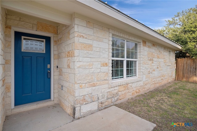 entrance to property featuring stone siding and fence