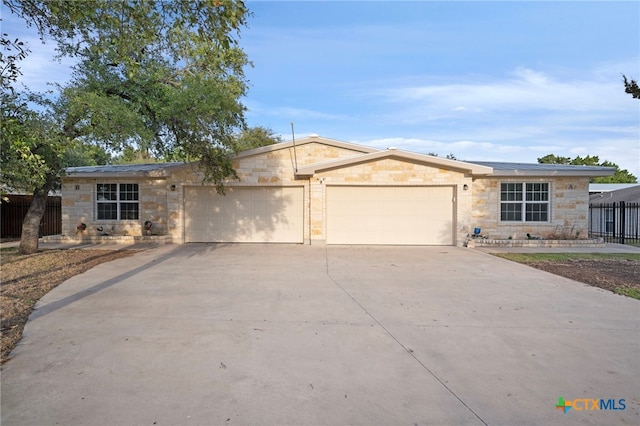 ranch-style home featuring a garage, concrete driveway, fence, and stone siding