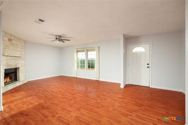 unfurnished living room with a stone fireplace, light wood-type flooring, and ceiling fan