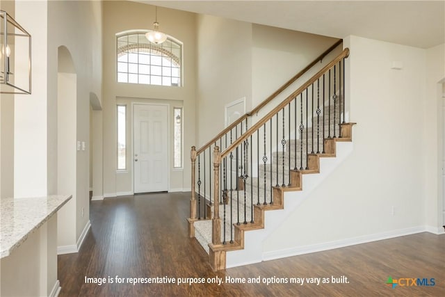 foyer entrance featuring a towering ceiling and dark wood-type flooring