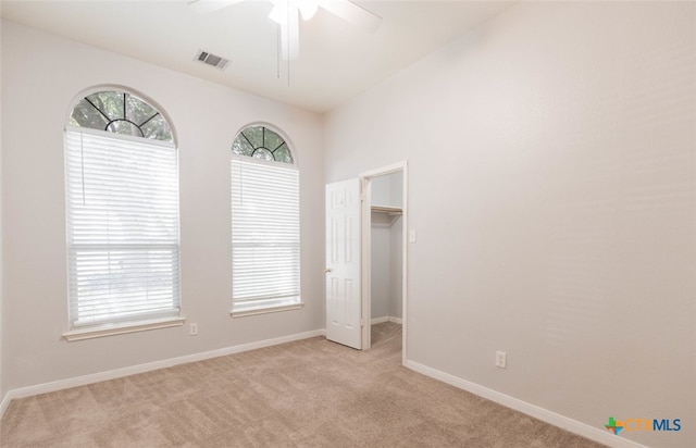 unfurnished bedroom with ceiling fan, light colored carpet, visible vents, baseboards, and a spacious closet