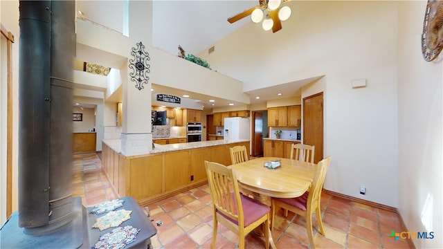 dining space featuring ceiling fan, a wood stove, and high vaulted ceiling