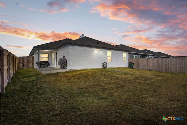 back house at dusk featuring a yard and a patio area