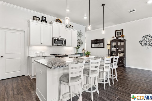 kitchen featuring white cabinetry, stainless steel appliances, hanging light fixtures, and an island with sink