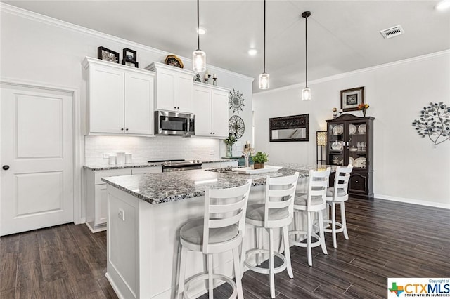 kitchen featuring stainless steel appliances, crown molding, decorative backsplash, dark wood-style floors, and a center island with sink