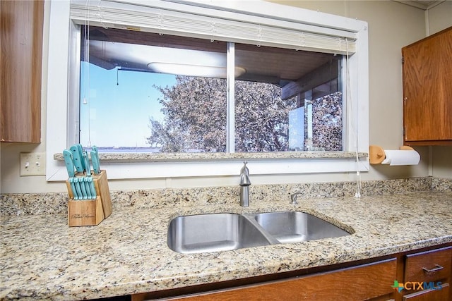 details with brown cabinets, light stone countertops, and a sink