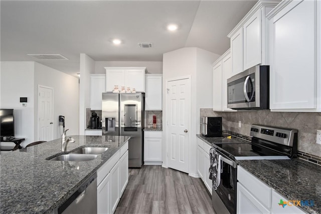 kitchen featuring white cabinets, stainless steel appliances, dark stone counters, decorative backsplash, and sink