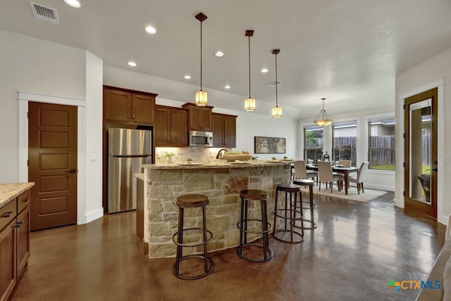 kitchen with stainless steel appliances, tasteful backsplash, a breakfast bar area, a kitchen island with sink, and pendant lighting