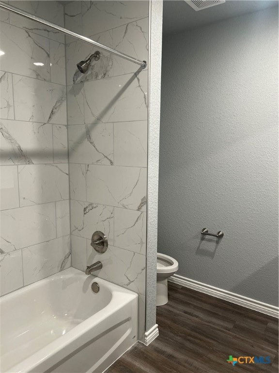 bathroom with tiled shower / bath combo, hardwood / wood-style flooring, and toilet