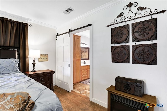 bedroom with a barn door, wood finished floors, visible vents, ornamental molding, and a sink
