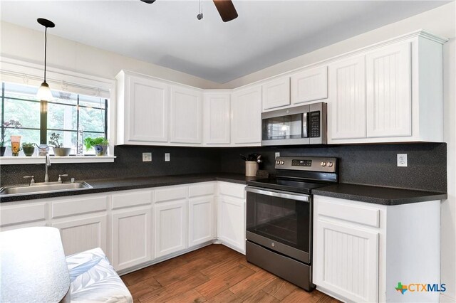 kitchen featuring dark countertops, a sink, stainless steel appliances, backsplash, and white cabinetry