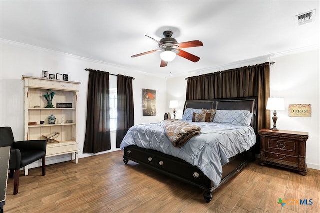 bedroom with wood finished floors, visible vents, and ornamental molding
